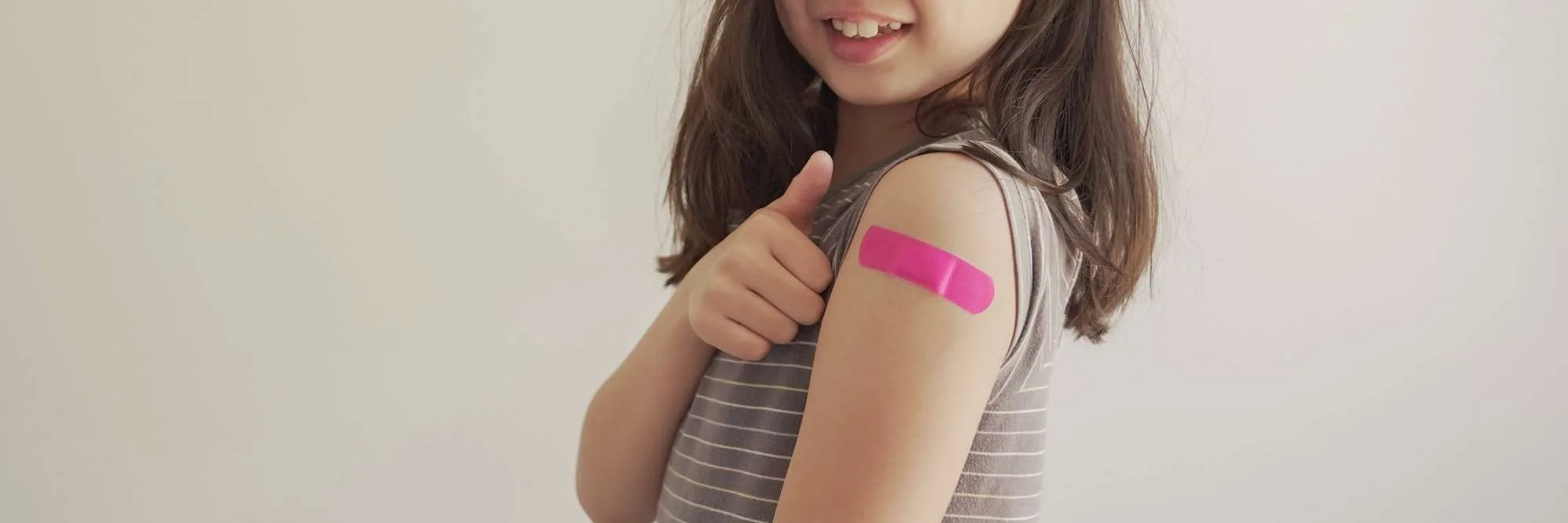 Mixed Asian girl showing arm with bandage after got vaccinated, child immunization