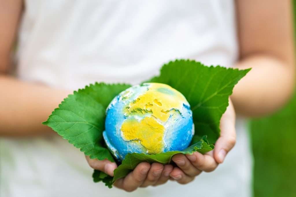 Kid holding small planet in hands against spring or summer green background. Ecology, environment